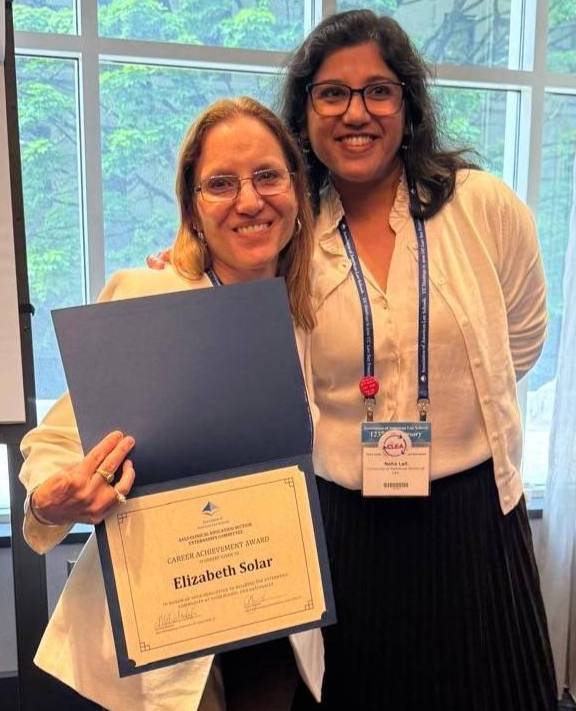 Two people pose together indoors, with one holding a certificate during an award recognition event.