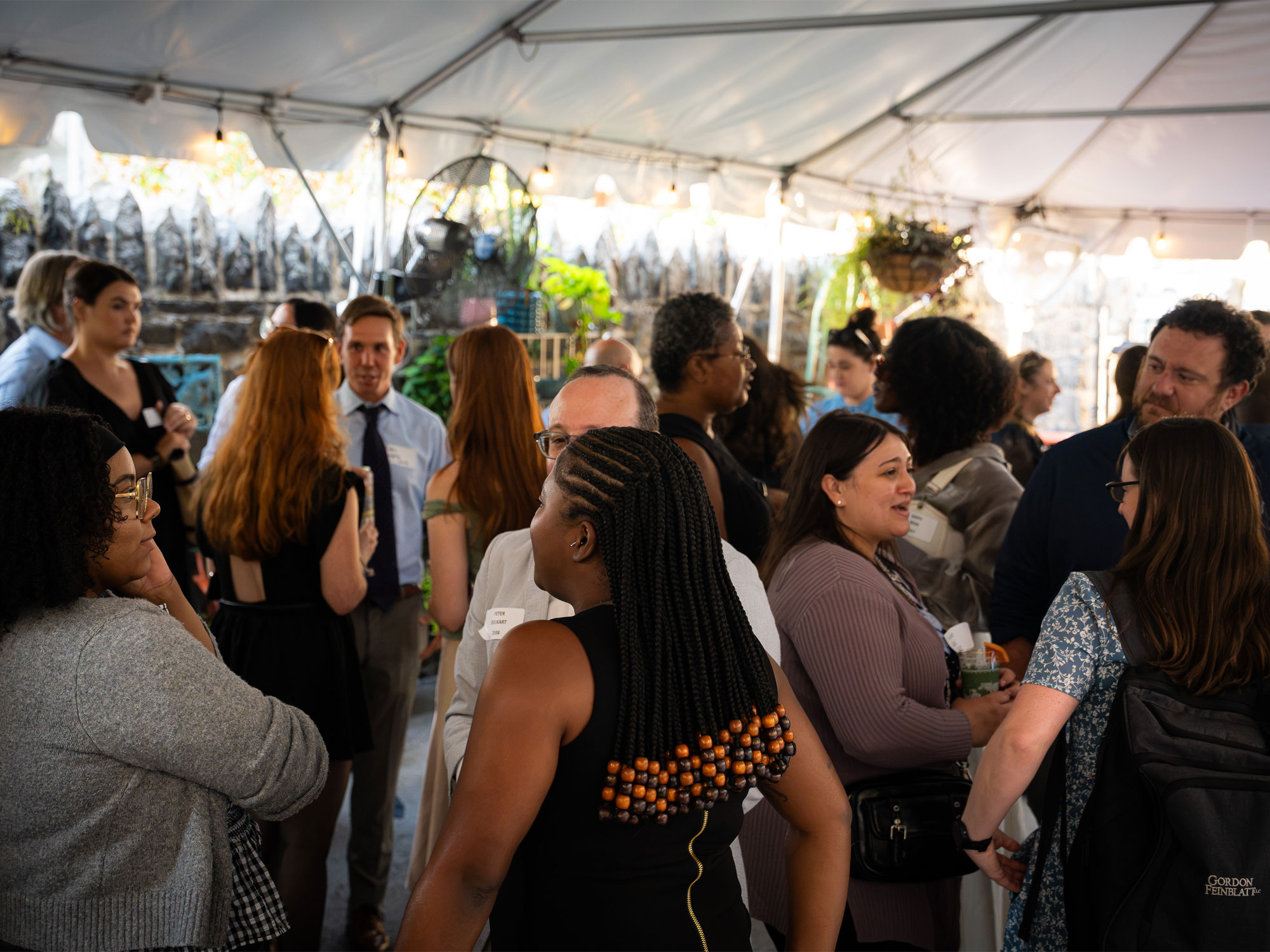 A group of UBalt Law community members socialize and network during an event under a tent.
