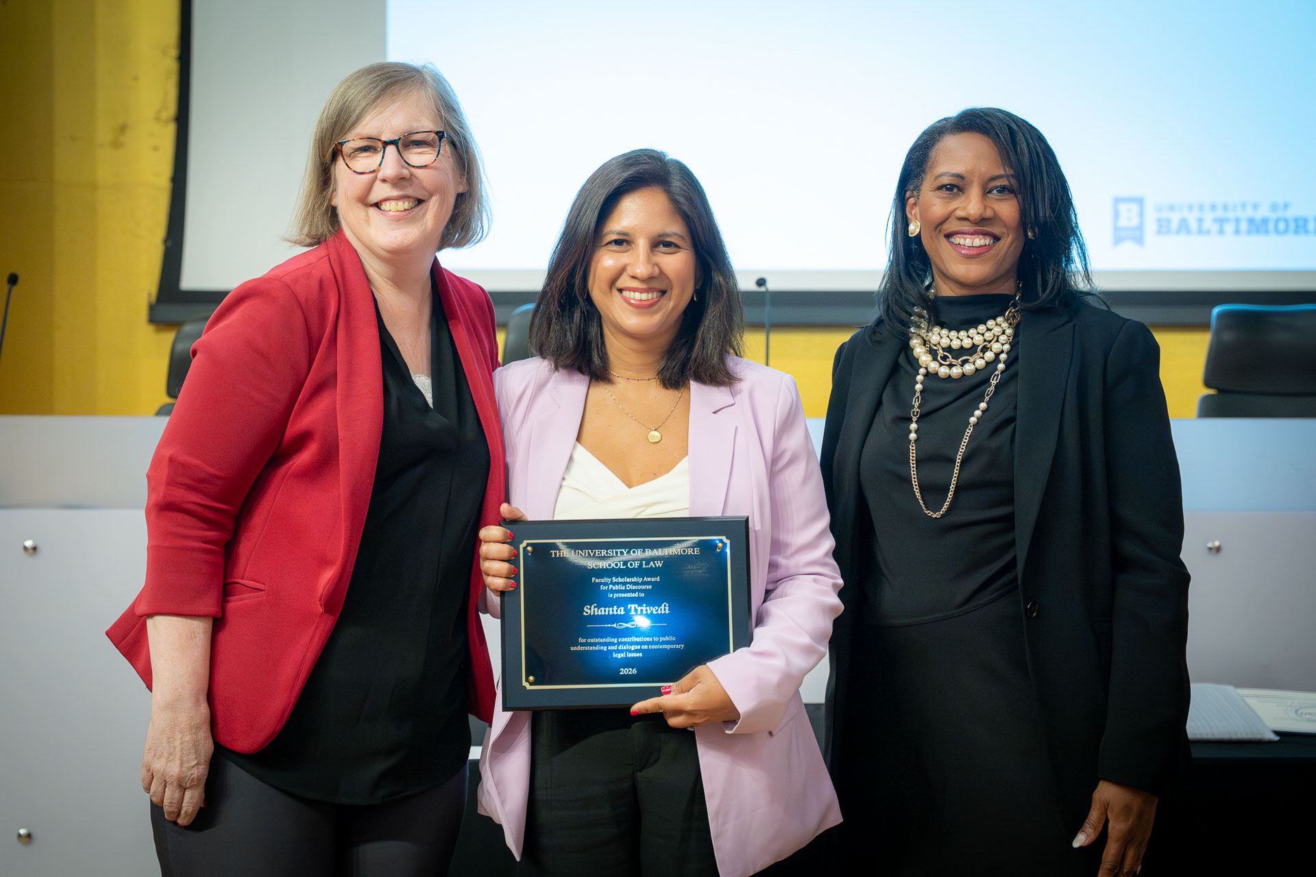 Three people pose together during a University of Baltimore School of Law awards ceremony, with one recipient holding an award plaque.