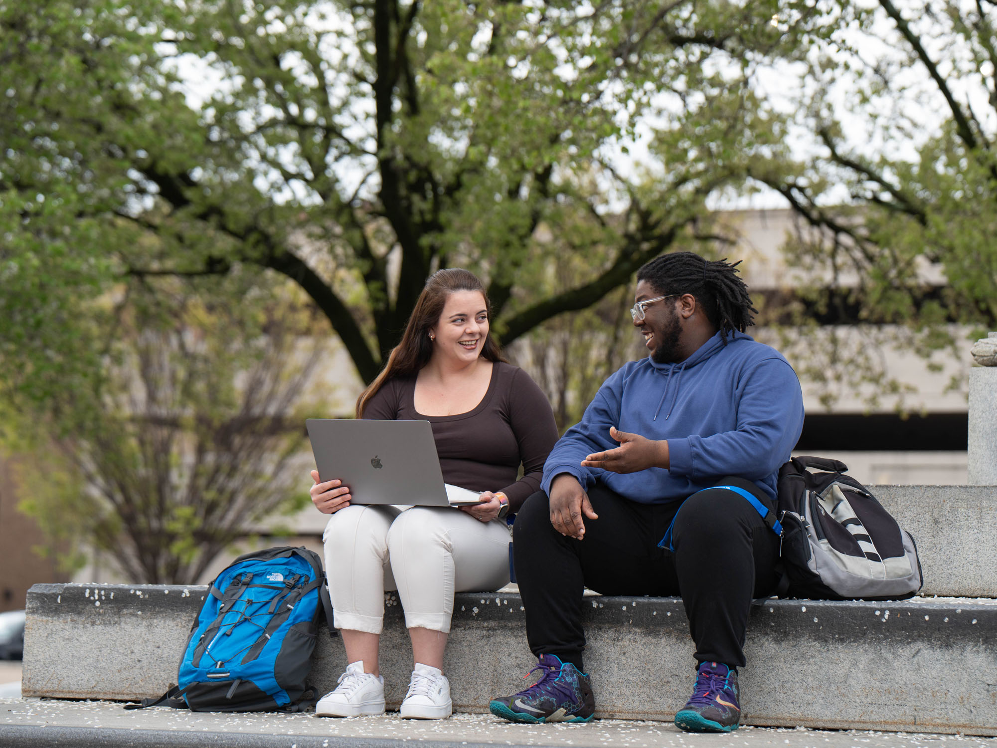 Two students sit talking on steps to a statue near campus