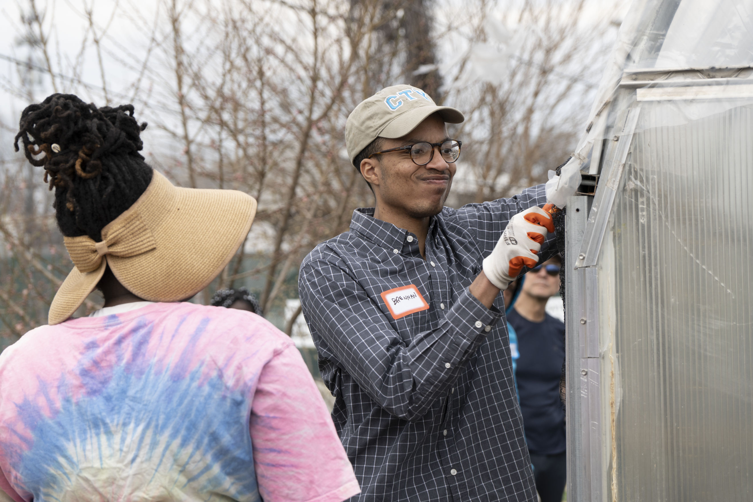 A student, with coaching from a farm manager, makes a face while working hard to remove old wire from a greenhouse at the farm.