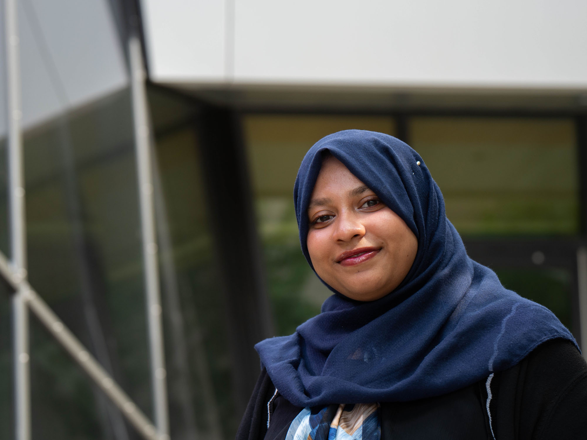 Wardha smiles looking at the camera while standing in an outdoor atrium at The University of Baltimore campus.