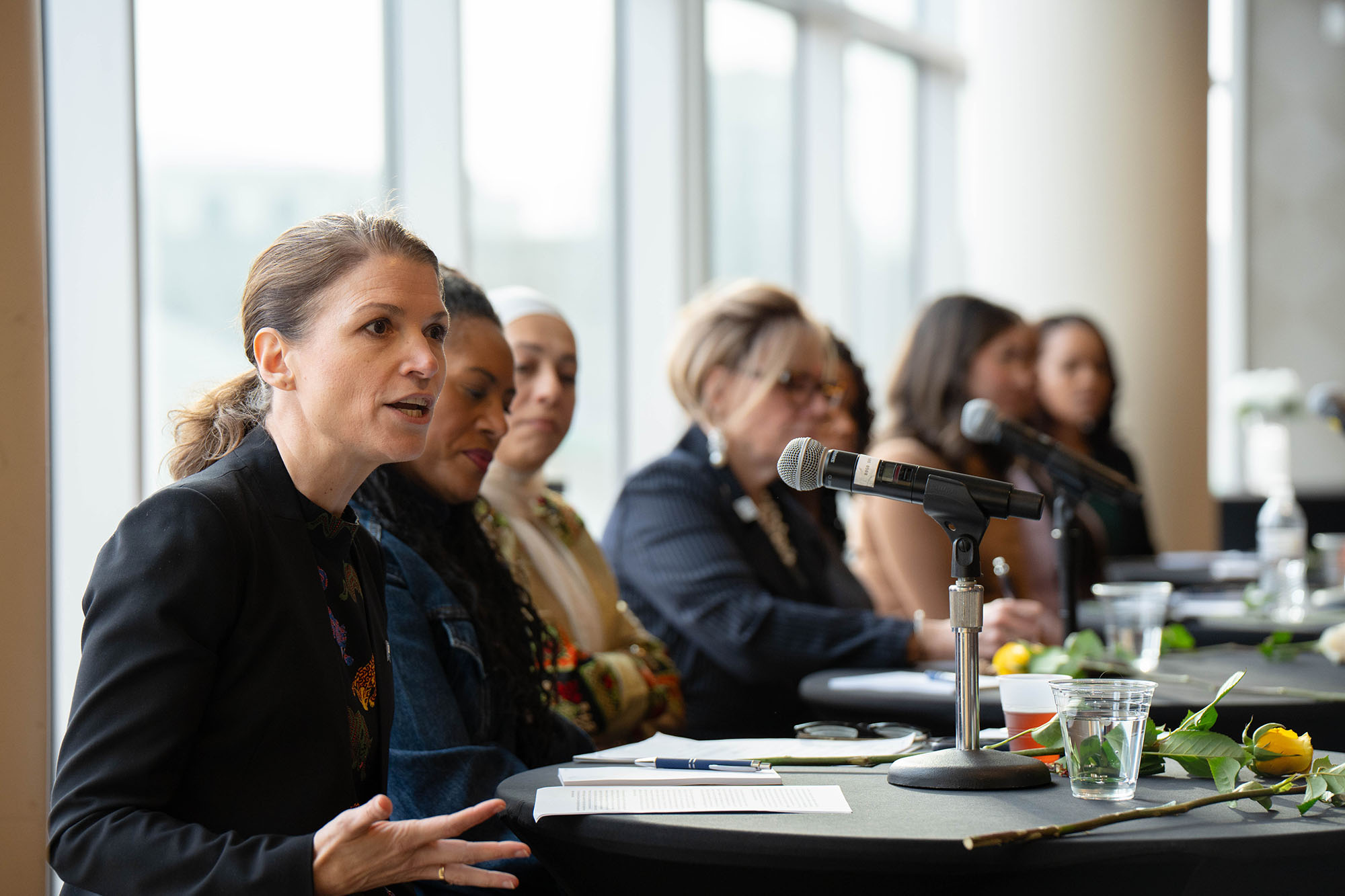 Jennica Larrison speaks to the audience during an International Women's Day celebration while the panel of women speakers looks on.