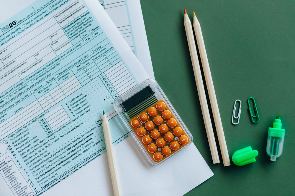Tax forms, a calculator, two pencils, paper clips, and a highlighter arranged on a green desktop.