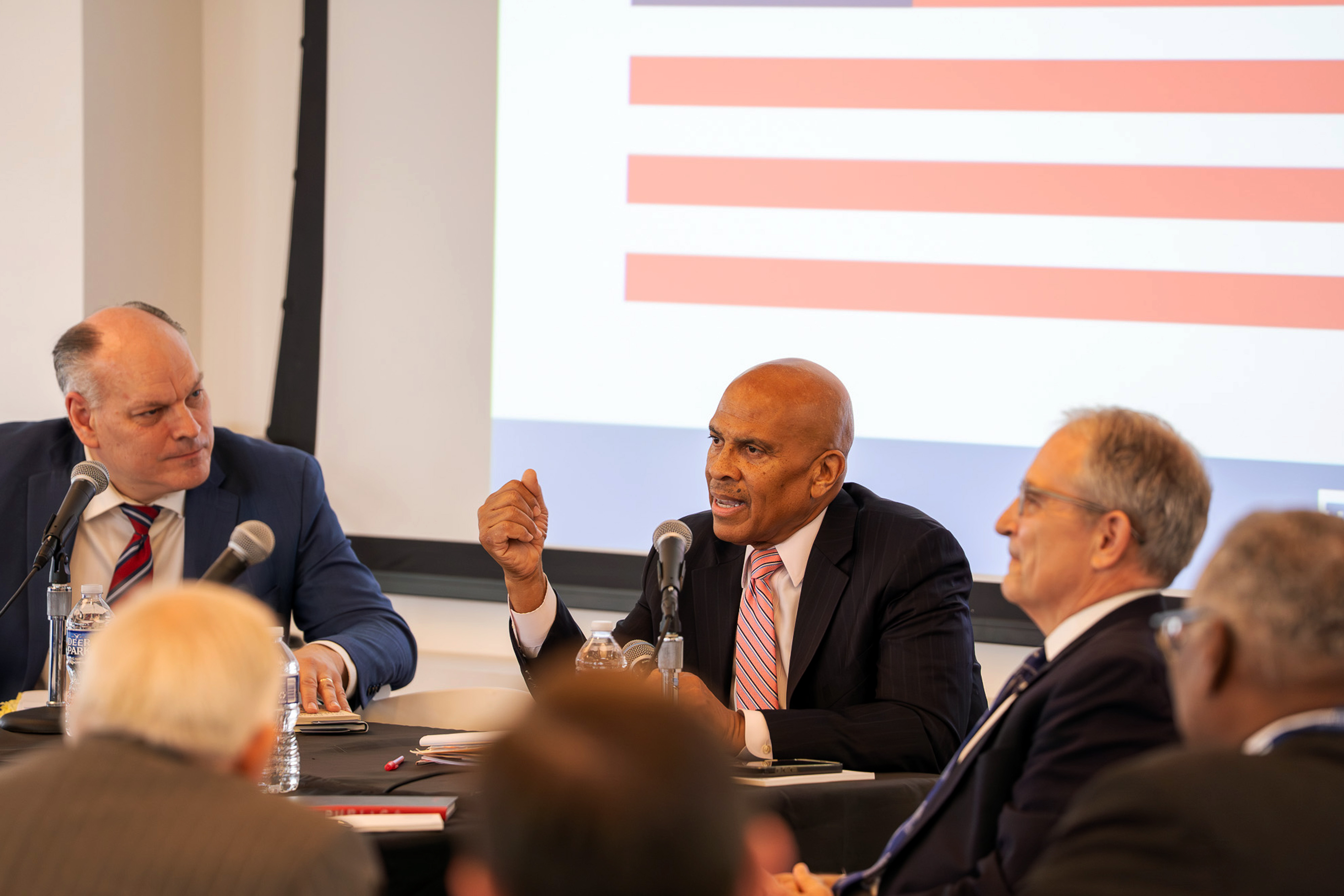 A panelist gestures while speaking into a microphone as fellow panelists listen during a discussion marking the 250th anniversary of the Declaration of Independence.