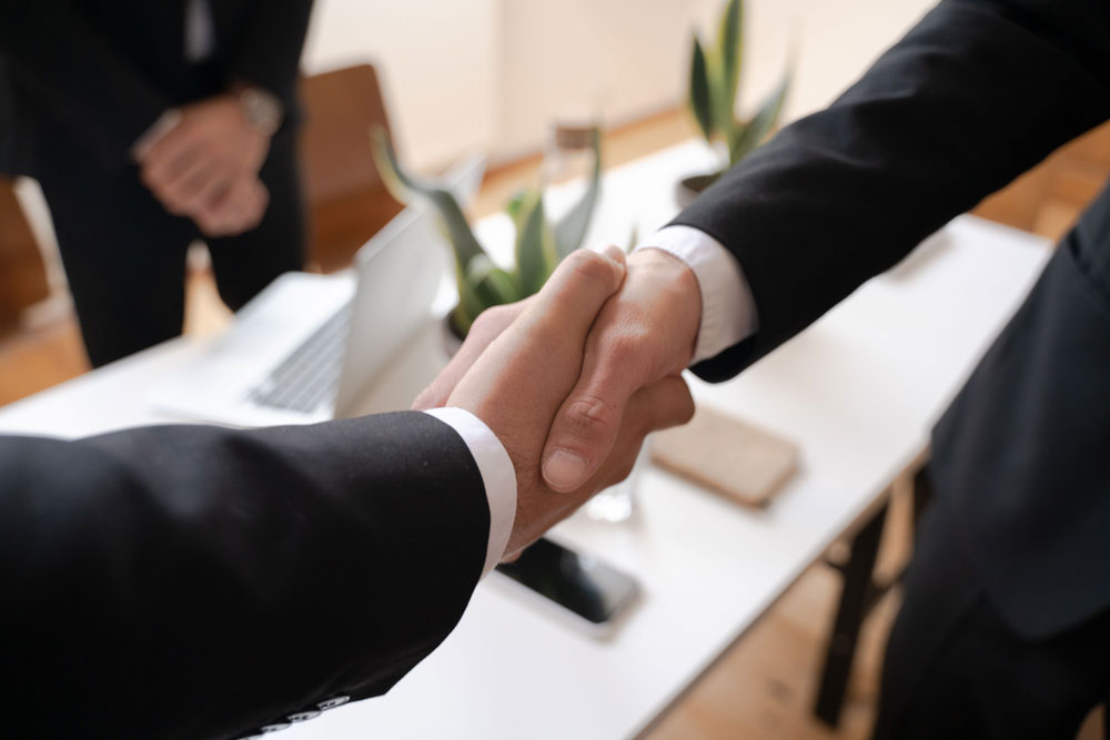 Two professionals shake hands across an office desk