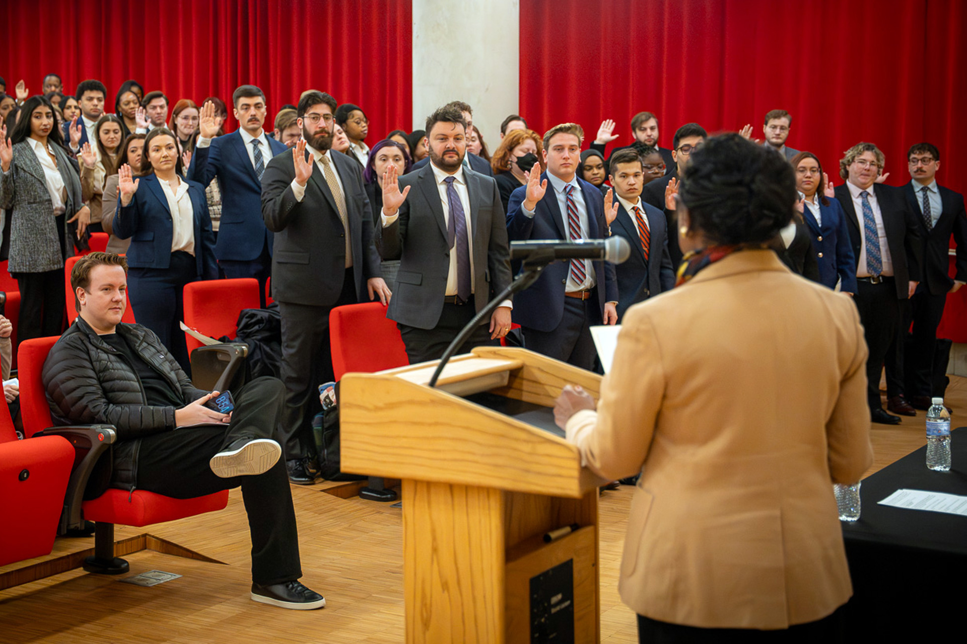 University of Baltimore School of Law students raise their right hands during a swearing-in ceremony led by an official at a podium.