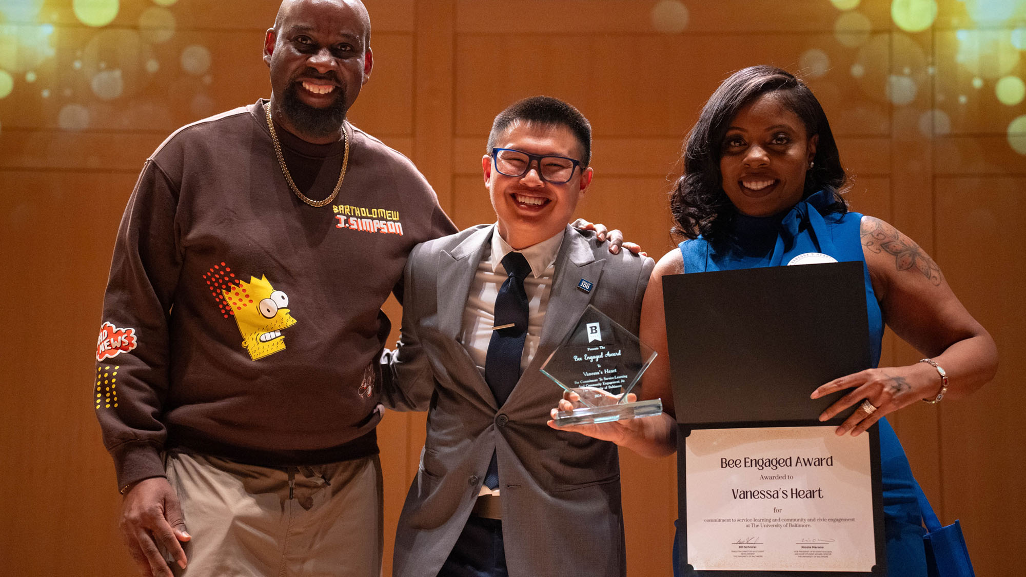 The presenter smiles while standing between two honorees, one holding the awards.