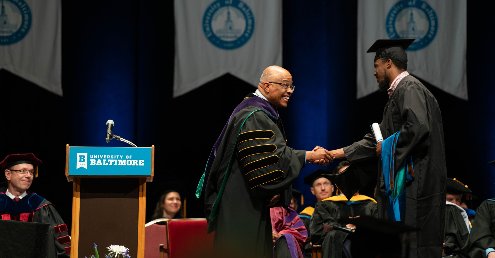 During the commencement ceremony, the president shakes hands with a graduate on stage.
